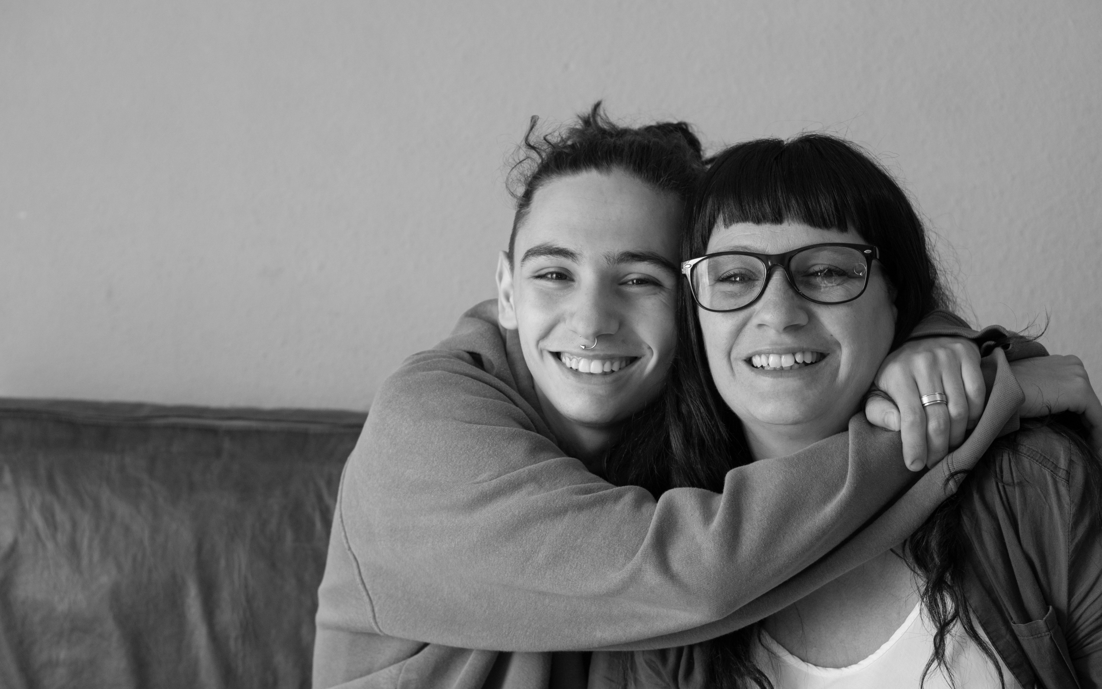 Two older people hugging and smiling towards camera.